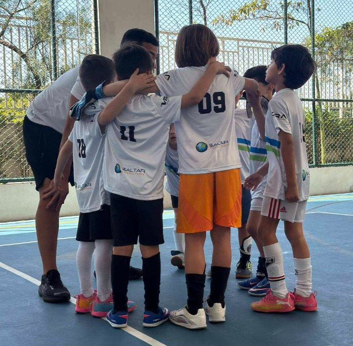 Crianças em roda com o treinador, uniforme com a marca da $altar