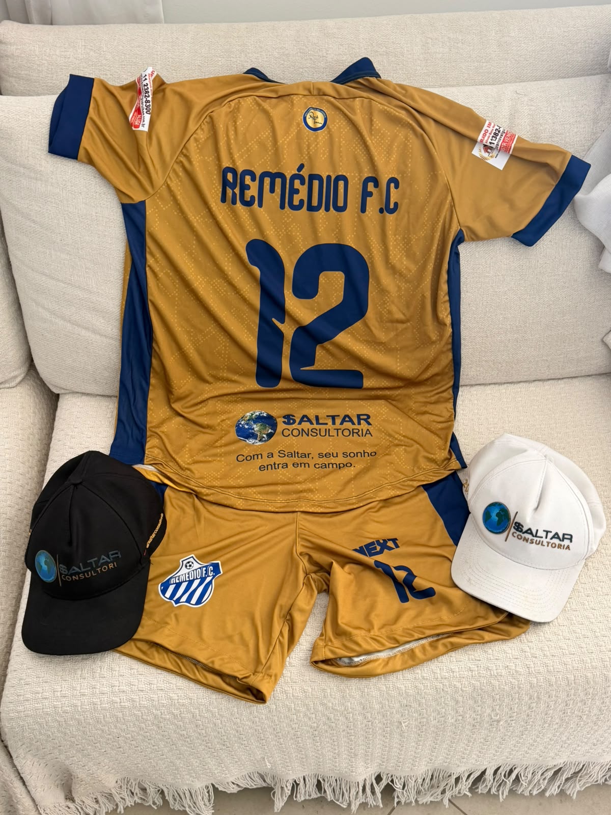 Uniforme dourado do Remédios Futebol Clube com a marca da $altar Consultoria e bonés